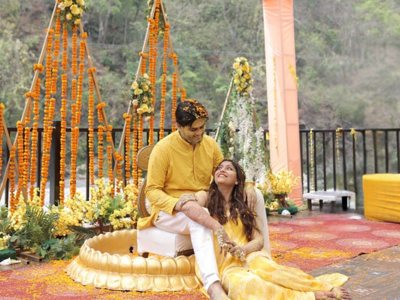 bride and groom seated in golden urns, surrounded by marigold floral decor during haldi ceremony