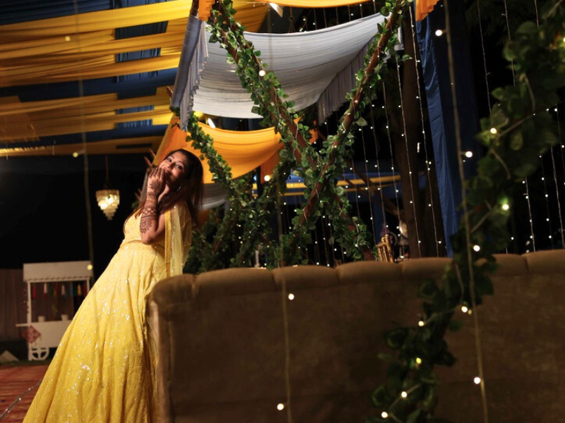 bride in a sparkling yellow lehenga posing joyfully in a vibrant setting with string lights