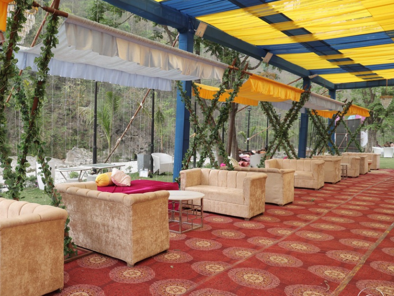 outdoor lounge setup with beige sofas and colorful cushions under a canopy decorated with greenery