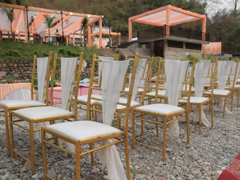 rows of gold chairs with white covers arranged on a pebbled riverside wedding venue