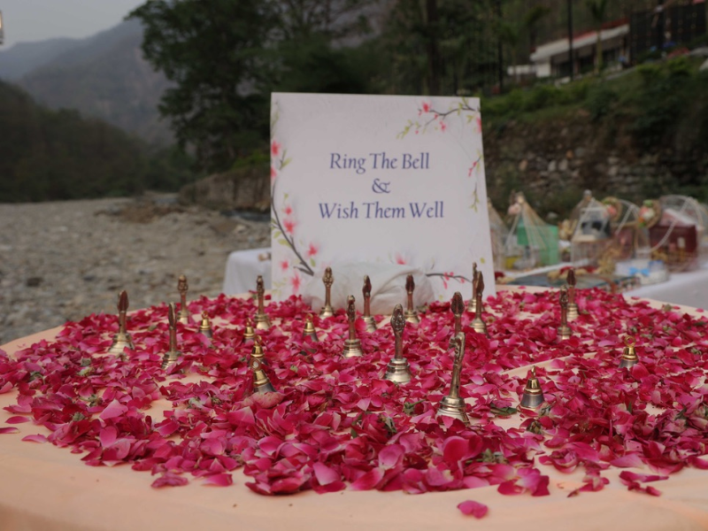 table adorned with bells and rose petals featuring a sign that reads ring the bell & wish them well