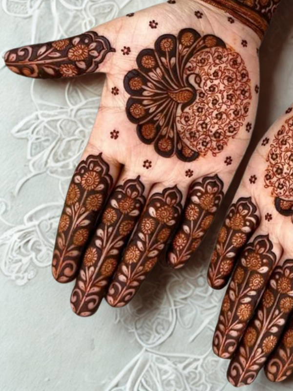 Elegant Mehndi design on the back of the hand featuring a detailed teardrop-shaped floral motif on the center, with intricate netted patterns and floral elements running along each finger