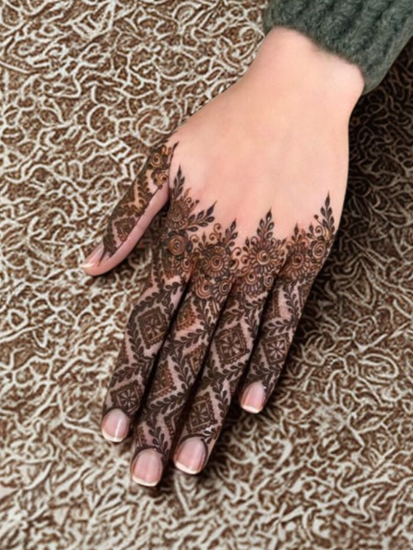 Elegant Mehndi design on the back of the hand featuring a detailed teardrop-shaped floral motif on the center, with intricate netted patterns and floral elements running along each finger