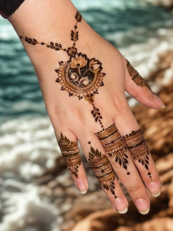 Intricate bridal Mehndi design on the back of the hand featuring a large circular mandala pattern connected to the wrist with dotted chains, and symmetrical scalloped motifs extending over the fingers