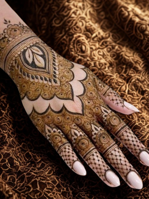 Intricate bridal Mehndi design on the back of the hand featuring a large circular mandala pattern connected to the wrist with dotted chains, and symmetrical scalloped motifs extending over the fingers