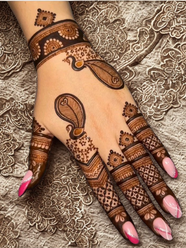 Intricate bridal Mehndi design on the back of the hand featuring a large circular mandala pattern connected to the wrist with dotted chains, and symmetrical scalloped motifs extending over the fingers