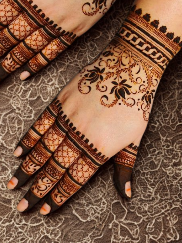 Intricate bridal Mehndi design on the back of the hand featuring a large circular mandala pattern connected to the wrist with dotted chains, and symmetrical scalloped motifs extending over the fingers
